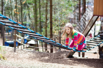 Child in adventure park. Kids climbing rope trail.