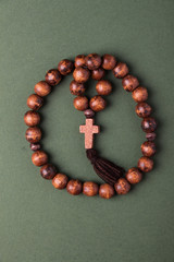 Wooden  rosary and cross on green background.