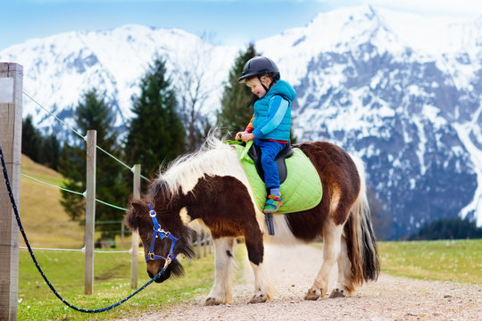 Kids riding pony. Child on horse in Alps mountains