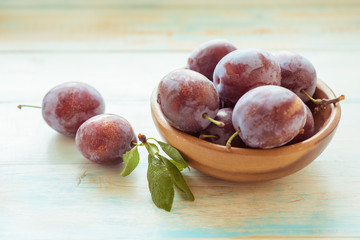Fresh plums in wooden bowl on table