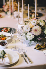 Banquet table for dinner decorated with flower bouquets of dahlia and white candles. On the table, glasses, cutlery and white plates