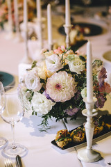 Banquet table for dinner decorated with flower bouquets of dahlia and white candles. On the table, glasses, cutlery and white plates