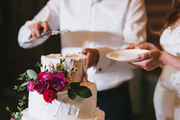 The bride and groom hold a plate and knife and cut the wedding cake with flowers and white cream
