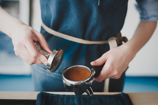The Barista girl prepares coffee, filling the receiver with ground coffee, pressing and making a tablet for the coffee machine. Side view with copy space for your text.