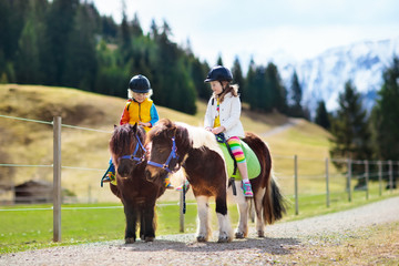 Kids riding pony. Child on horse in Alps mountains