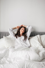 sexy young brunette woman wearing a white shirt on the bed at home. Girl's morning