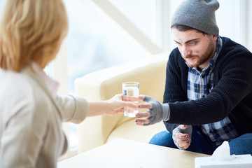 Obraz premium Young homeless man or migrant taking glass of water from hand of social worker before talk
