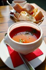 Fresh made vegetables cream soup served in white bowl with bread on outdoor terrace in sunlight
