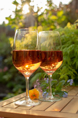 Two cold rose wine glasses served on outdoor terrace in garden with flowers in sunny day