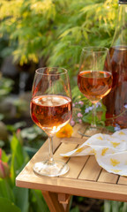 Cold rose wine in glasses served on outdoor terrace in garden with flowers in sunny day