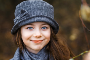 A close up portrait of a girl in grey coat and a cute gray hat in the forest in early spring. A girl outside after rain at the sunset