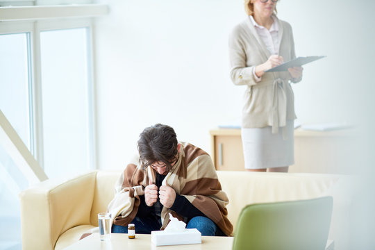 Victim of natural disaster sitting on sofa in front of table and receiving psychological help in the center of social support