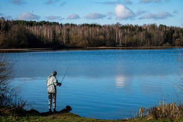 Fototapeta na wymiar Man fishing rod on the shore of the pond in the woods