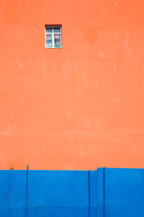Orange wall of a house with one window Contrast with a blue fence. Back background Texture