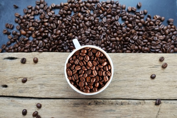 Roasted coffee beans texture with coffee beans scattered on dark background and white cup – top view
