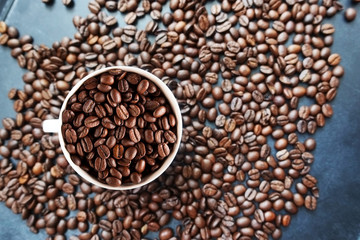 Roasted coffee beans texture with coffee beans scattered on dark background and white cup – top view

