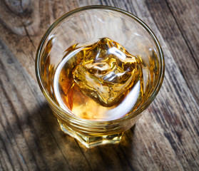 top view of glass of whiskey with ice on wooden background