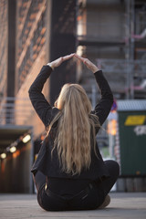 Mujer sentada delante de un edificio en obras haciendo el signo de casa con sus manos.
