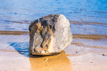 Stone on the sandy shore of the lake in summer day