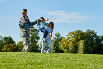 Soldier and his family having fun outdoors. Playing on the grass in the park. Warm summer sunny day.