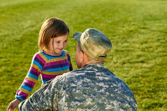 US army soldier with little daughter in park. Close up little girl with father in military uniform in green grass background.