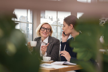 Talking about project. Joyful blond businesswoman drinking tea and her partner taking on the phone