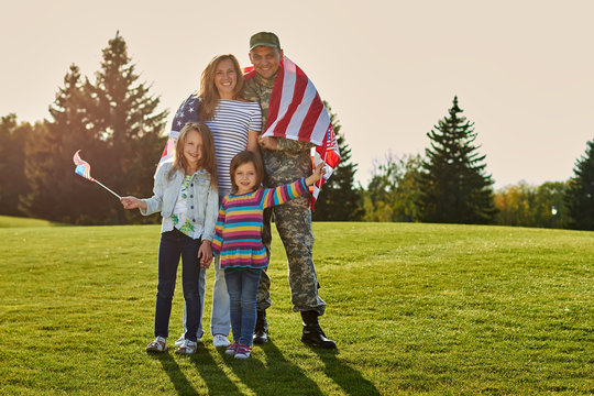 Shot of patriotic family. Soldier with his wife and daughters with american flags.