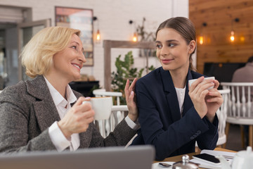 Good job. Delighted successful businesswomen talking and drinking coffee