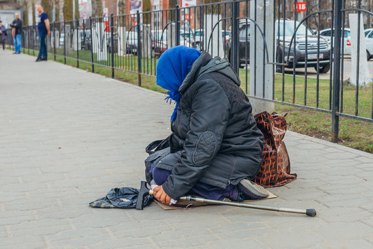 Old homeless woman is sitting on street and begging money 