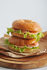 Beagle with salted salmon, salad and soft cheese filling. Beagles on kraft paper and on a round wooden board. Light background. Close-up. Vertical orientation of the frame.