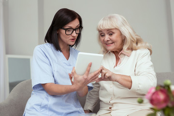 New technology. Appealing elder woman learning to use tablet while nurse holding it