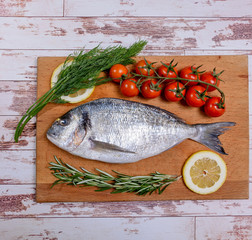 Fresh dorado fish with cherry tomatoes, rosemary and lemon on wooden cutting board