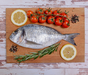 Fresh dorado fish with cherry tomatoes, rosemary and lemon on wooden cutting board