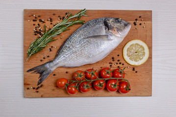 Fresh dorado fish with cherry tomatoes, rosemary lemon and pepper on wooden cutting board