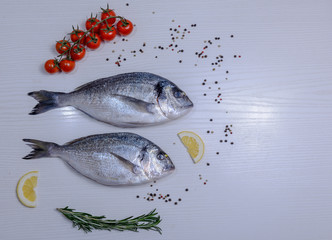 Two fresh dorada fishes with cherry tomatoes, rosemary, lemon and pepper on light wooden background