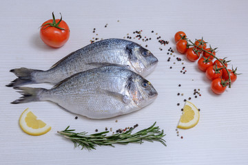 Two fresh dorada fishes with cherry tomatoes, rosemary, lemon and pepper on light wooden background