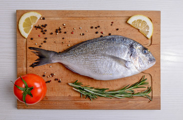 Fresh dorado fish with tomatoe, rosemary, lemon and pepper on wooden cutting board