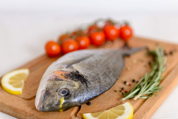 Fresh dorado fish with cherry tomatoes, rosemary, lemon and pepper on wooden cutting board