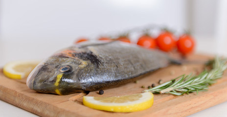 Fresh dorado fish with cherry tomatoes, rosemary, lemon and pepper on wooden cutting board