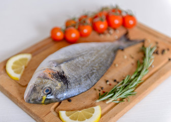 Fresh dorado fish with cherry tomatoes, rosemary, lemon and pepper on wooden cutting board