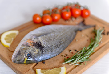 Fresh dorado fish with cherry tomatoes, rosemary, lemon and pepper on wooden cutting board