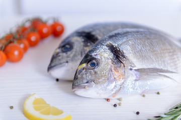 Two fresh dorada fishes with cherry tomatoes, rosemary, lemon and pepper on light wooden background close up