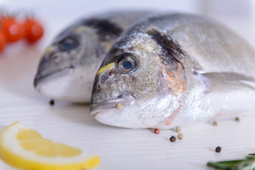 Two fresh dorada fishes with cherry tomatoes, rosemary, lemon and pepper on light wooden background close up