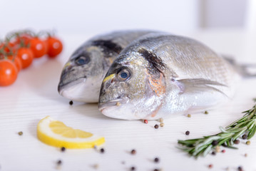 Two fresh dorada fishes with cherry tomatoes, rosemary, lemon and pepper on light wooden background...