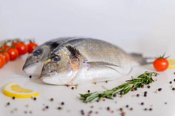 Two fresh dorada fishes with cherry tomatoes, rosemary, lemon and pepper on light wooden background close up