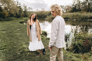 A beautiful couple in free clothes walks in the lawn near the lake on a sunny summer day