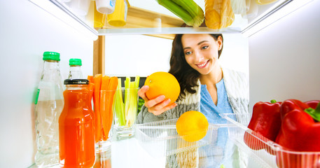 Portrait of female standing near open fridge full of healthy food, vegetables and fruits. Portrait of female