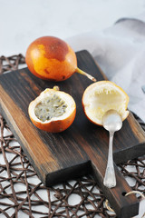 Granadilla is an exotic tropical fruit. Two fruits lie on a wooden board. One of the fruits is cut in half. In the frame cutlery. Close-up. Vertical orientation of the frame.