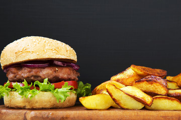 American burger with fried potatoes on wooden board. Closeup.