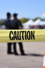 Caution tape with police officers in background blurred